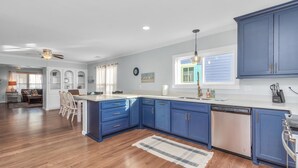 Eine moderne Küche mit blauen Schränken, einem Geschirrspüler und einem Essbereich mit einem Holztisch und Stühlen.
