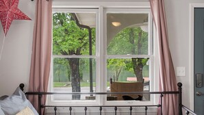 A bedroom with a large window, a bed with pillows, and a view of trees and a bench outside. - Herons Lake View Hideaway (Rockaway Beach)
