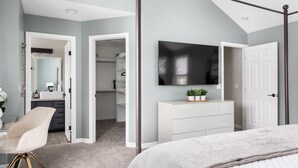 Une chambre avec un grand lit, un téléviseur fixé au mur, un dressing et une salle de bain avec un miroir et un lavabo.