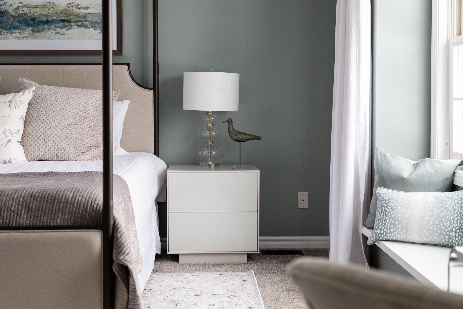 A neatly arranged bedroom with a bed, bedside table, lamp, and decorative bird.
