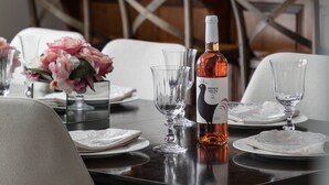 Une table à manger dressée avec des assiettes, des verres et une bouteille de vin, avec des meubles en bois et une chaise à croisillons en arrière-plan.