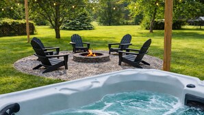 Un bain à remous avec un foyer et quatre chaises Adirondack, le tout installé dans un jardin.