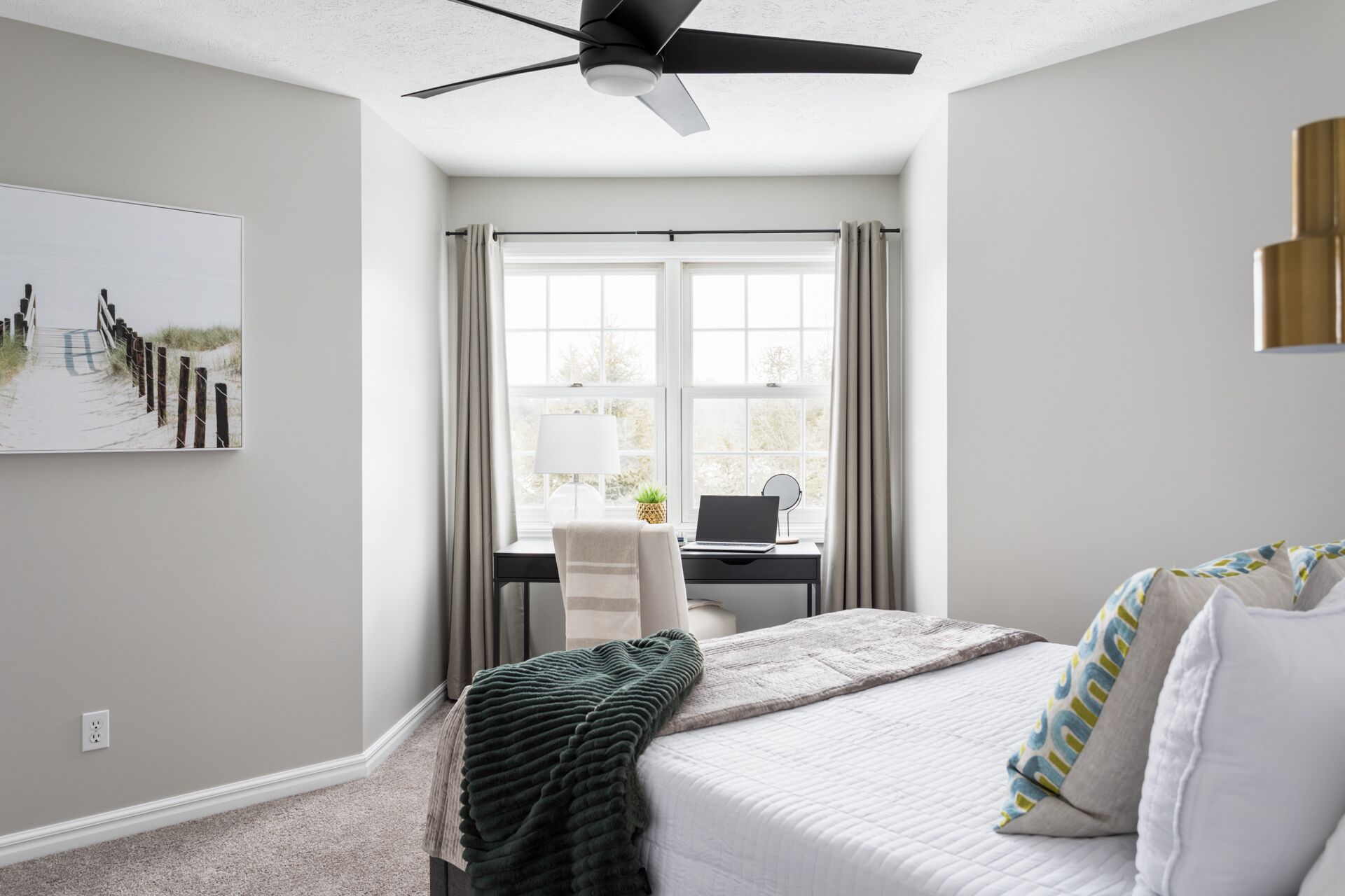 Une chambre à coucher avec un lit, un bureau, un ordinateur portable, un ventilateur de plafond et une fenêtre avec des rideaux.
