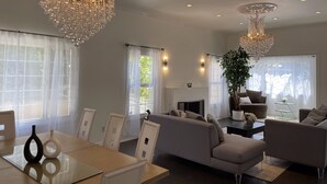 Een ruime woonkamer met een grote bank, een eettafel met stoelen en twee kroonluchters.