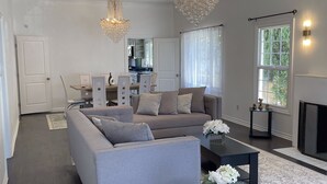 Een ruime woonkamer met een grijze bank, een zwarte salontafel en een kroonluchter.