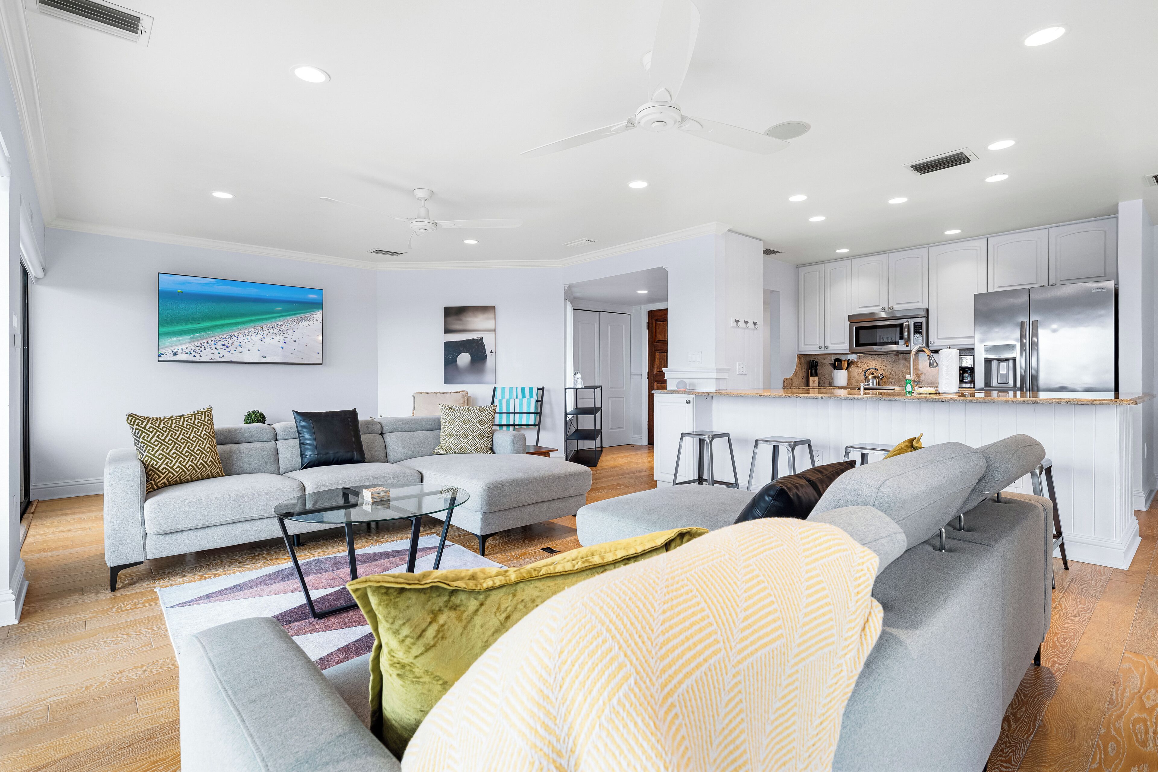A modern living room with a grey sofa, a glass coffee table, and a yellow throw pillow.