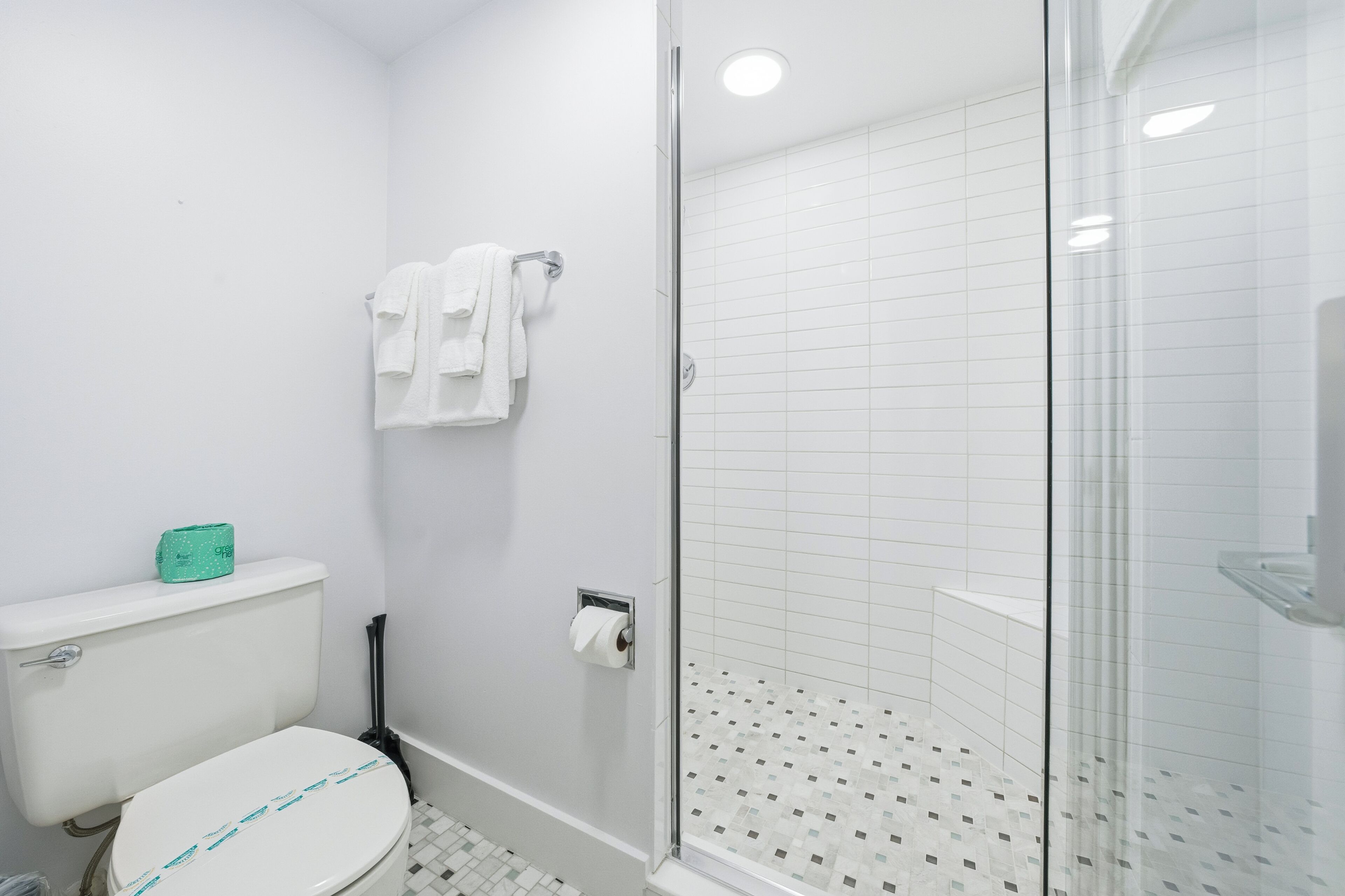 Ein Badezimmer mit Toilette, einer Duschkabine aus Glas und einem Handtuchhalter mit mehreren Handtüchern.