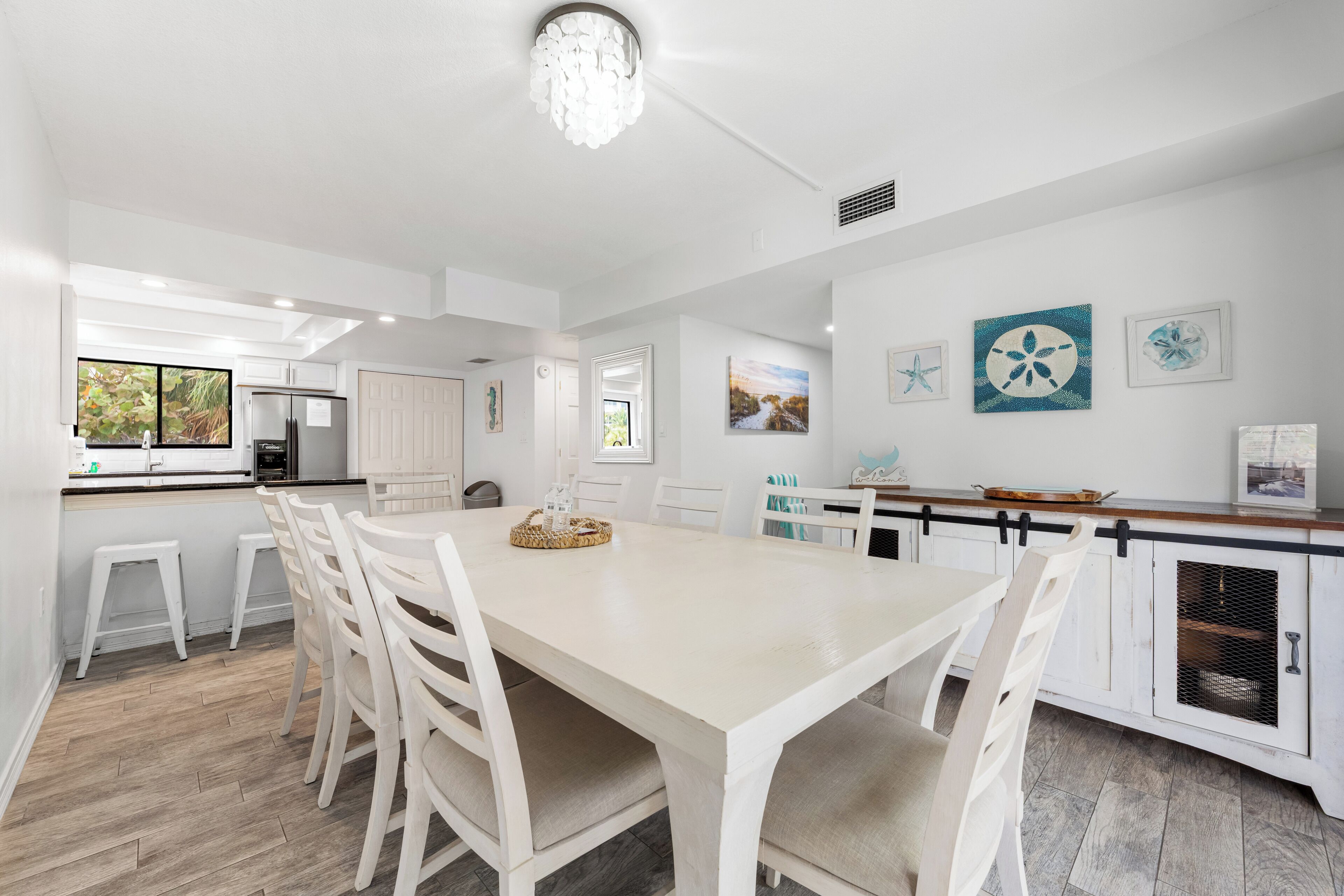 Una cocina moderna con armarios blancos, un comedor con una mesa grande y sillas, y obras de arte en las paredes.