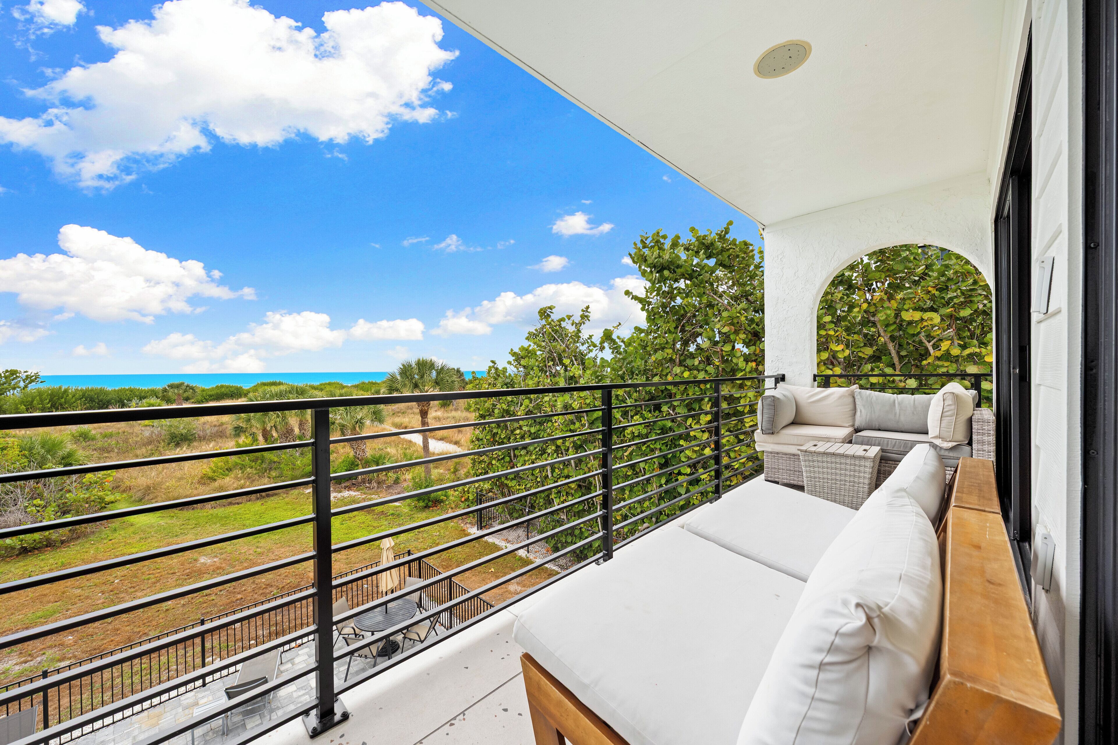 A balcony with a white sofa and wooden bench, overlooking a grassy area and trees.