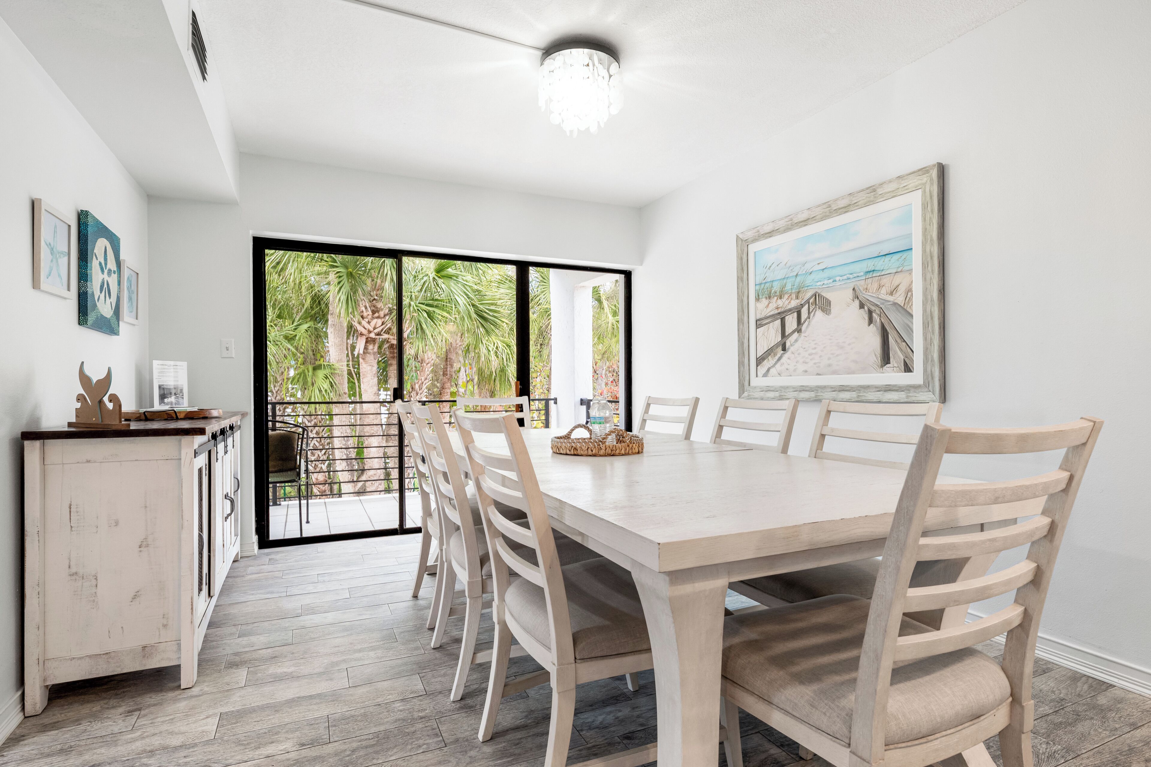 A dining area with a large table and chairs, a cabinet, and a painting of a beach scene.