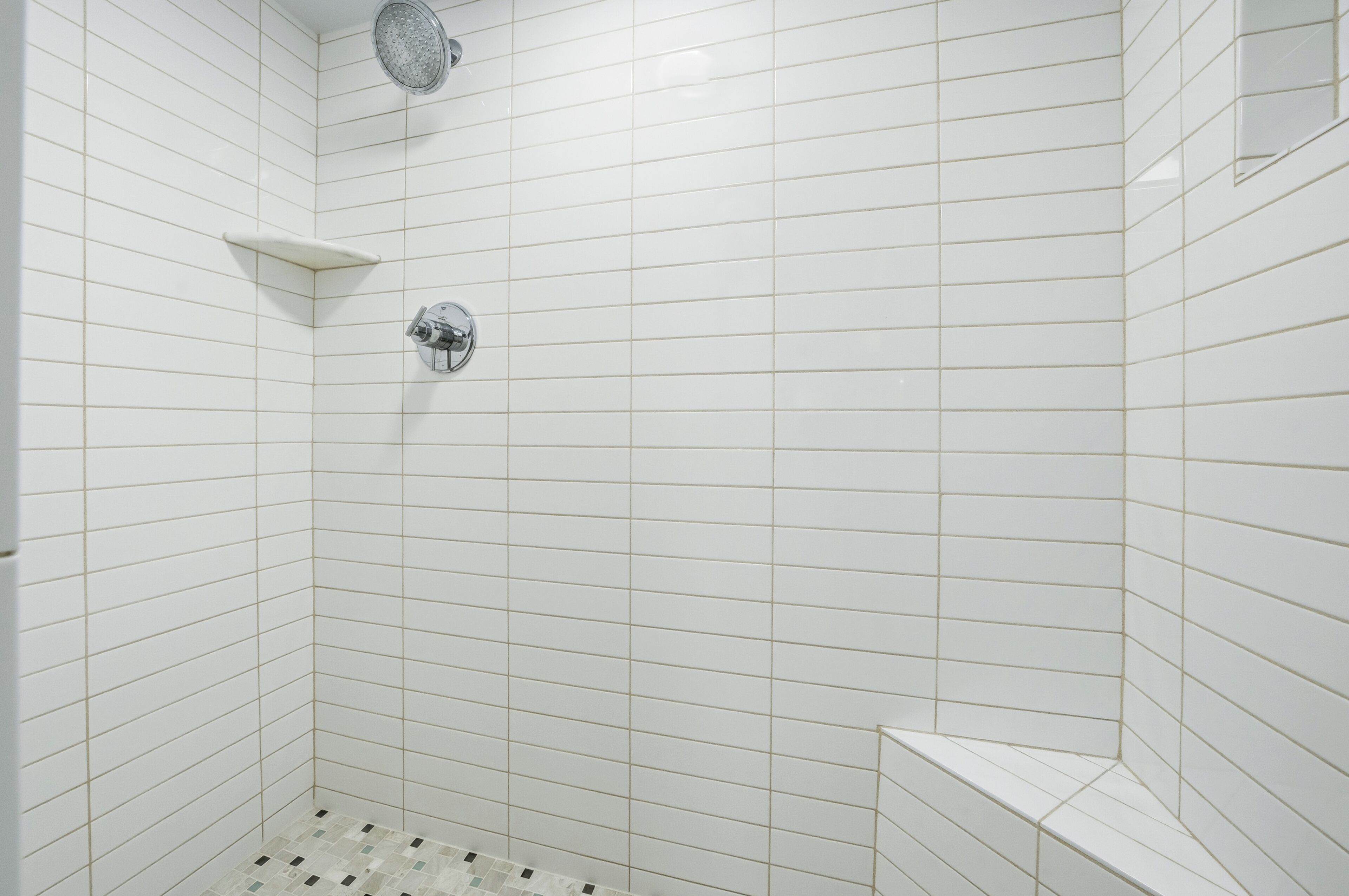 A bathroom with white tiled walls and a shower area.