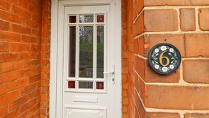 A white door with a glass panel, a small mailbox, and a house number plaque on a brick wall. - Coastguard Cottages (Hull)