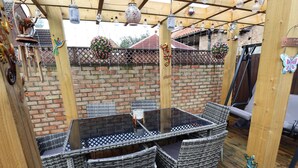 An outdoor patio with wicker furniture, a glass-top table, and hanging decorations. - Coastguard Cottages (Hull)
