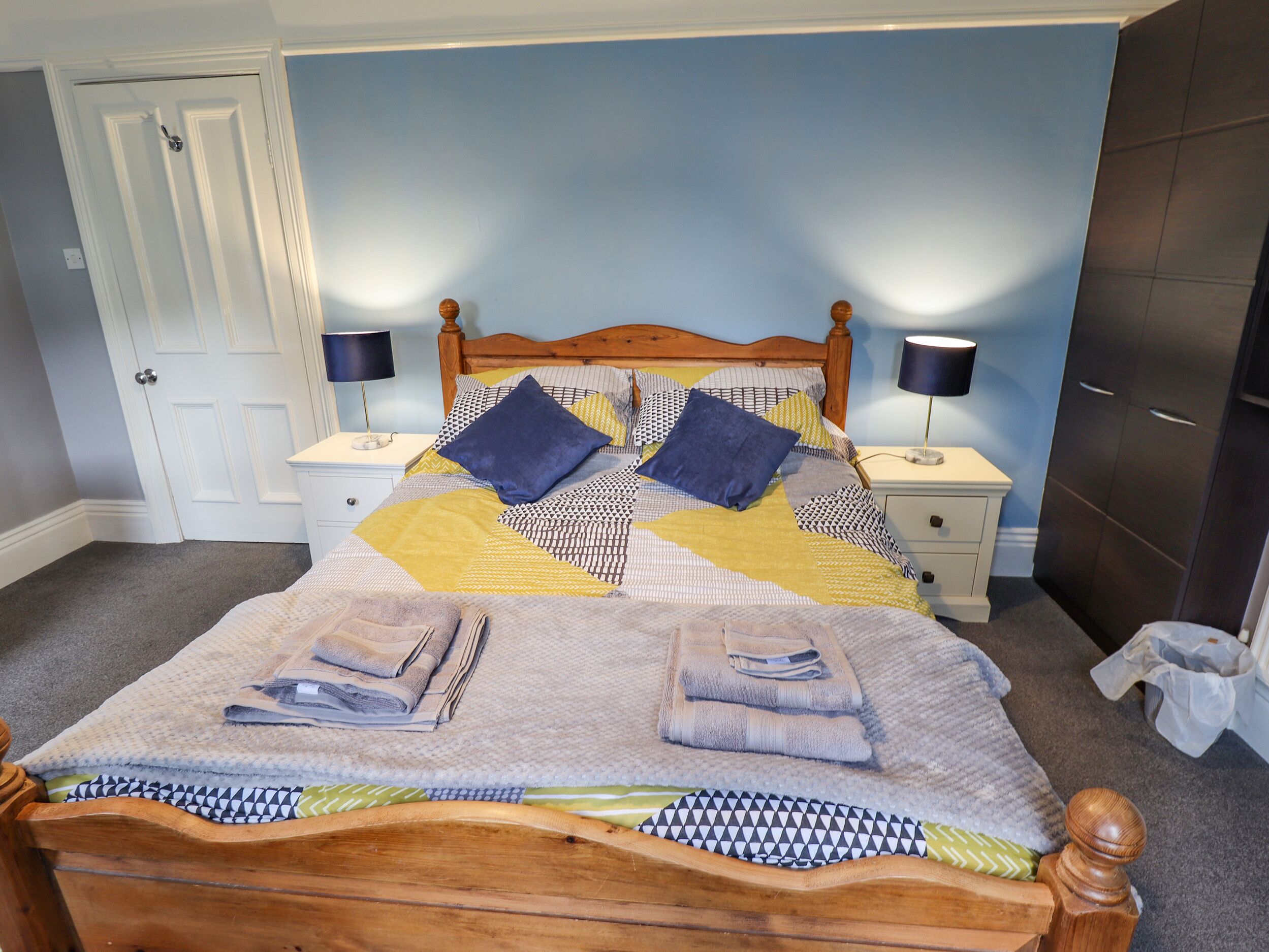A neatly made bed with a patterned quilt, two bedside lamps, and a wooden headboard.