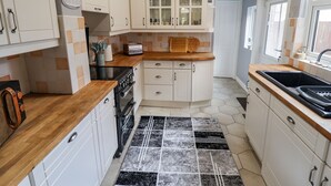 A kitchen with white cabinets, a wooden countertop, a black stove, and a tiled backsplash. - Coastguard Cottages (Hull)
