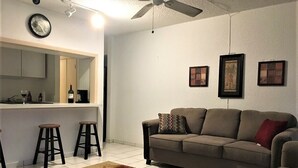 Sala de estar com sofá cinza, dois banquinhos, tapete estampado e ventilador de teto.
