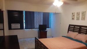 Um quarto com uma cama, uma televisão em móvel, uma janela com cortinas e um ventilador de teto.