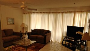 Uma sala de estar com sofá, mesa de centro, televisão e ventilador de teto.