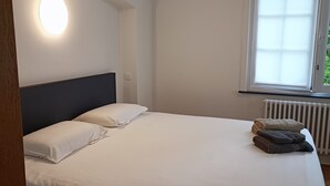 A bedroom with a bed, a round wall light, a window, and a radiator. - Pearl in the heart of Bruges (Brugge)