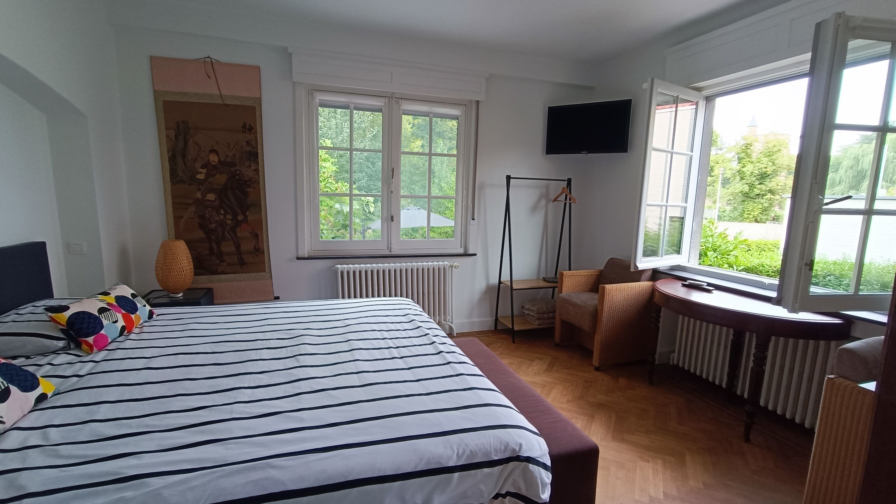 A bedroom with a large bed, a television, and a window with a view of greenery.