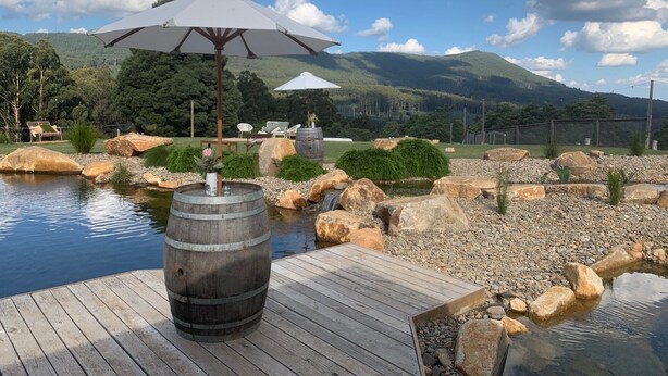 A wooden deck with a barrel, an umbrella, and a small water feature.