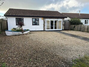 A house with a tiled roof, a gravel driveway, a boat in the garden, and a wooden fence.