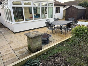 A patio with a table and chairs, a stone planter, and a conservatory with windows.