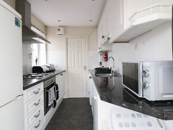 A modern kitchen with white cabinetry, a black countertop, a stove, a microwave, and a sink.