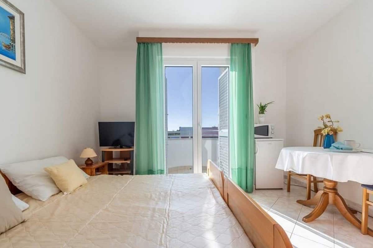 A bedroom with a bed, a TV, a small table with a plant, and a balcony with a view.