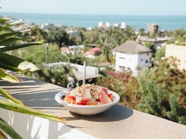 Un tazón de ensalada de frutas en un balcón con vistas a un pueblo costero.