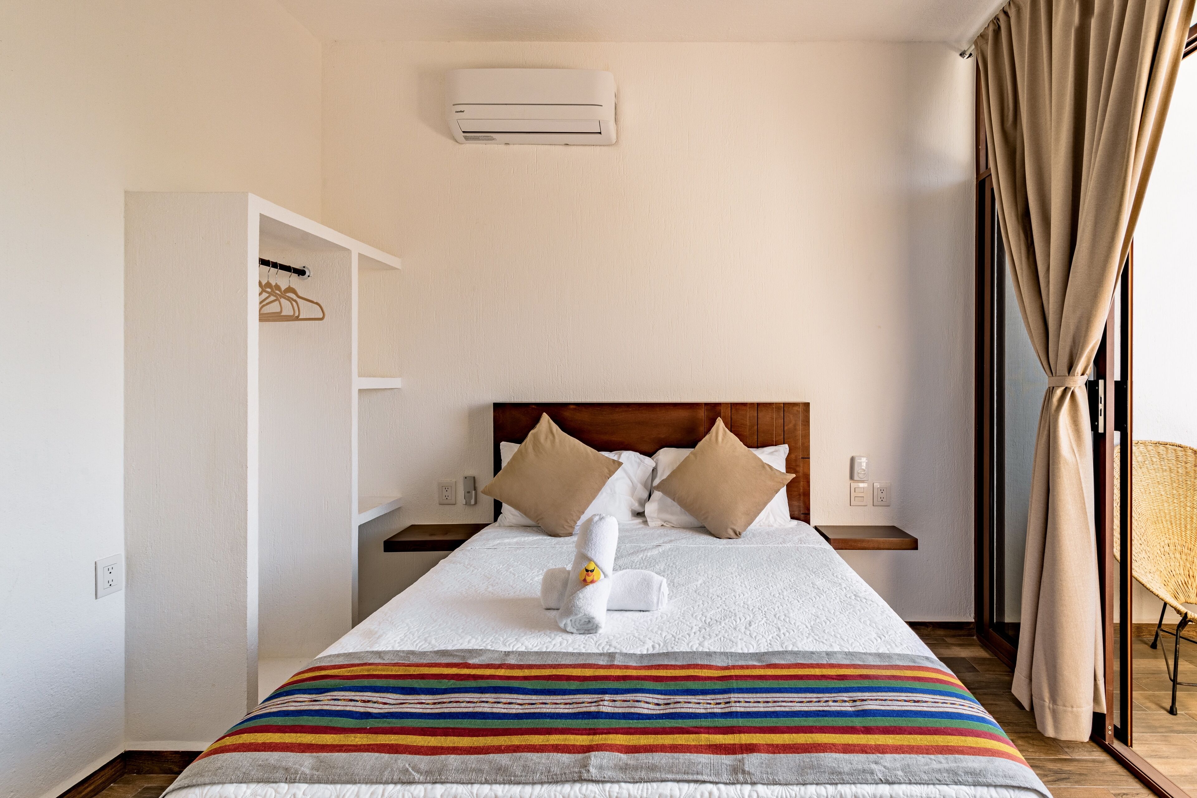 Una habitación de hotel con una cama, un armario, una mesita de noche y un aire acondicionado.
