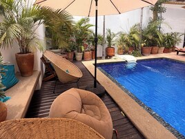 Zona junto a la piscina con una silla de descanso, una piscina pequeña y varias plantas en macetas.