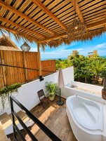 Una terraza en la azotea con cubierta de madera, una bañera blanca y vista al océano.
