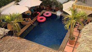 Una piscina con lettini e ombrelloni, circondata da piante in vaso.
