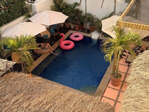 A swimming pool with lounge chairs and umbrellas, surrounded by potted plants. - PUNTA KAI  (Puerto Escondido)