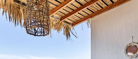 A balcony with a hot tub, a thatched ceiling, and a view of palm trees and the ocean.