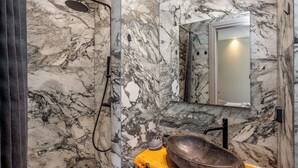 Une salle de bain avec un mur en marbre, une douche, un lavabo avec un receveur et un miroir.