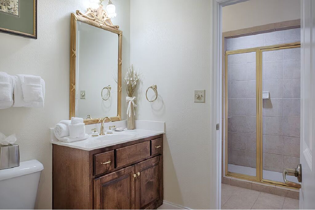 Un baño con tocador de madera, un espejo grande, ducha con puerta de cristal y toallas en la pared.