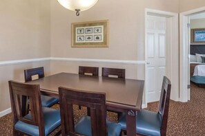 Un coin repas avec une table rectangulaire et six chaises, un tableau encadré au mur et une porte blanche en arrière-plan.