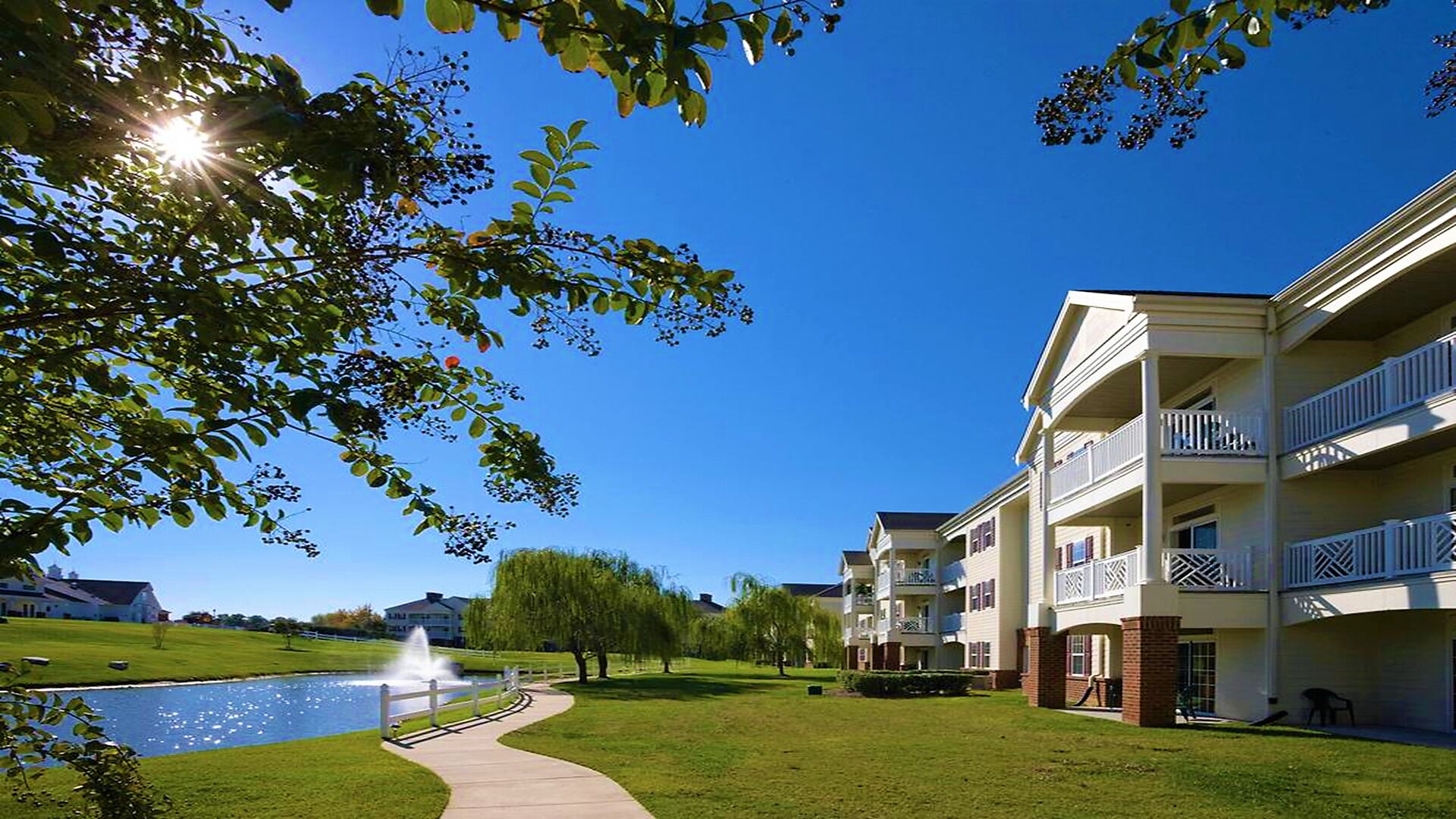 Um edifício residencial com várias varandas, piscina e um gramado bem cuidado.