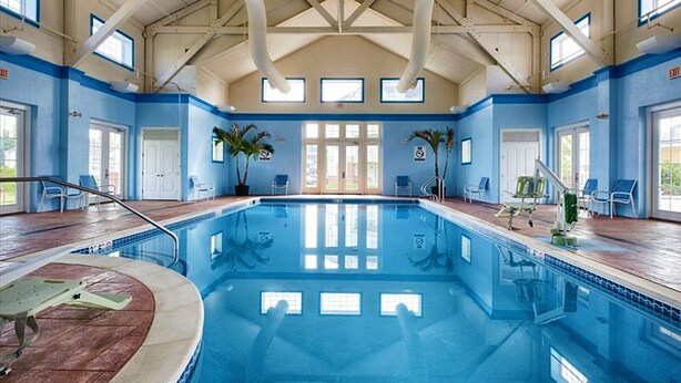 Een binnenzwembad met helderblauw water, omringd door blauwe wanden en een hoog plafond met zichtbare balken.