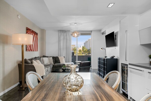 Una sala de estar moderna con una mesa de comedor, sofá y un amplio ventanal con cortinas.