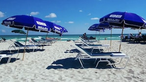 A beach with rows of sun loungers and blue umbrellas labeled "BOULAN" on a clear day.