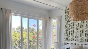 A bedroom with a bed, curtains, a ceiling fan, and a view of greenery outside. - Charming, light-filled home - walk to the beach! (Aptos)
