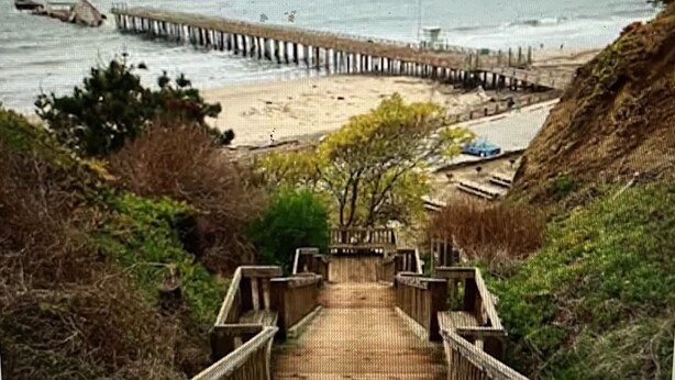 A wooden staircase leading to a beach with a pier extending into the water. - Charming, light-filled home - walk to the beach! (Aptos)