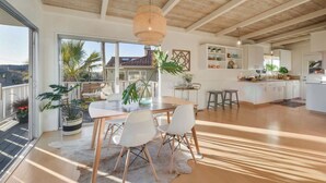 A spacious living area with a large dining table, white chairs, and a ceiling with exposed beams. - Charming, light-filled home - walk to the beach! (Aptos)