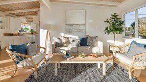 A living room with a sofa, coffee table, and wicker chairs. There is a large window with a view of the outdoors. - Charming, light-filled home - walk to the beach! (Aptos)