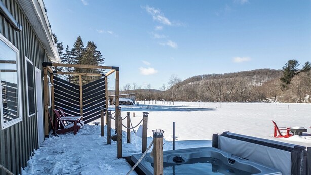 Un espace extérieur enneigé comprenant un bain à remous, une terrasse en bois et des fauteuils Adirondack.
