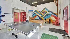 Une salle de loisirs équipée d’une table de ping-pong, d’un baby-foot et ornée d’une fresque colorée représentant un paysage de montagne.