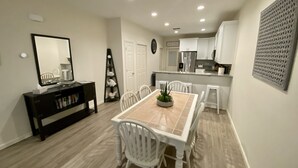 A modern kitchen with white cabinets, a stainless steel refrigerator, and a dining area with a wooden table and white chairs. - Set Sail 7 - Spacious Townhome 3 Bed/2.5 bath/sleeps7 - 1 min walk to the beach! (Mexico beach)